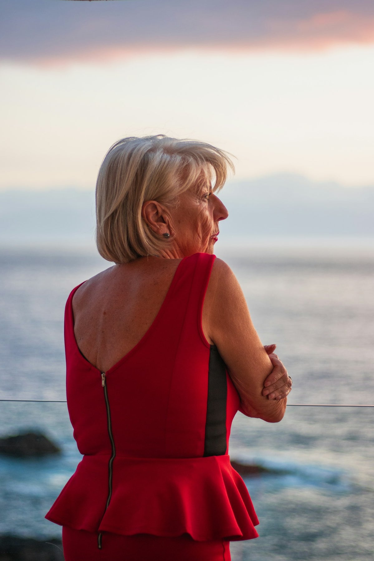 Woman in a red dress looking out to sea at sunset